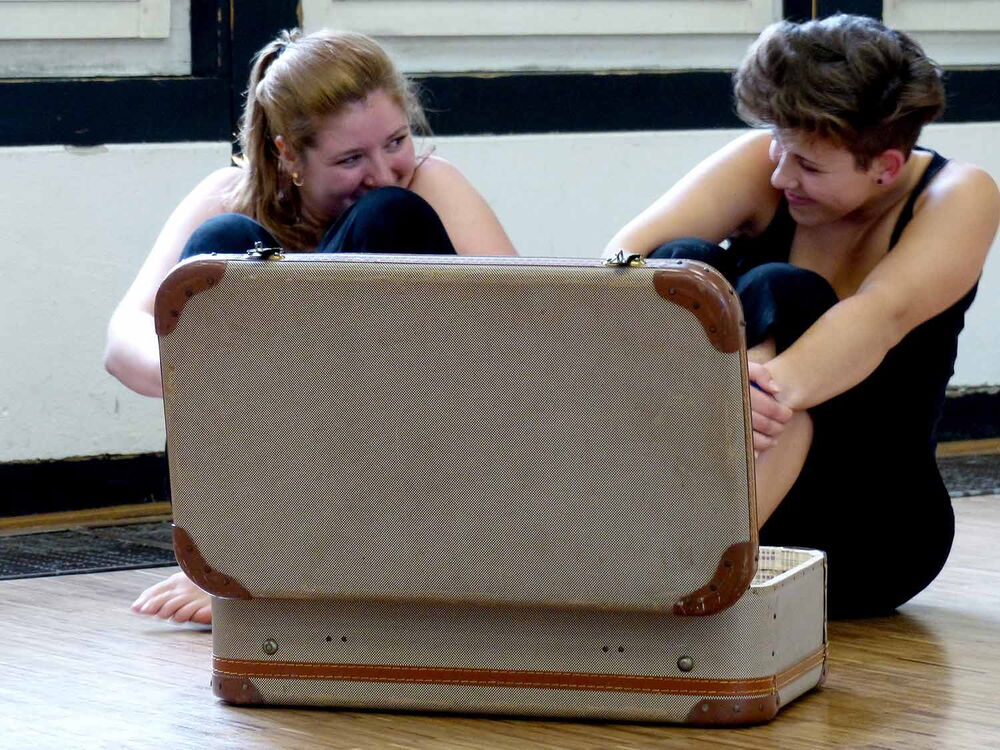 2 junge Frauen sitzen amüsiert vor einem offenen Koffer.