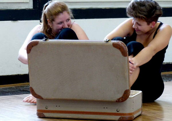 2 junge Frauen sitzen amüsiert vor einem offenen Koffer.