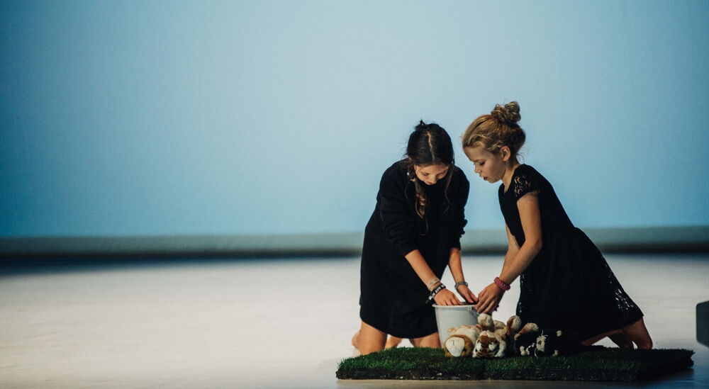 2 Mädchen knien vor einem Eimer, 1 Mädchen hält ihre Hände hinein