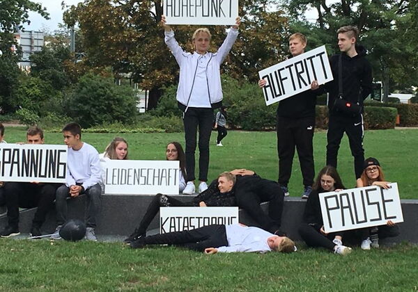 Mehrere junge Leute stehen, sitzen oder liegen auf einer Sitzmauer und halten Schilder