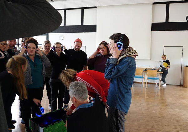 Mehrere Menschen in einem Raum haben Kopfhörer auf und hören sich etwas an